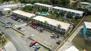A multi-story hotel with a parking lot, surrounded by greenery and hills. - Caribbean Blue Hideaway | 1BR Condo w/ Ocean View (Christiansted)