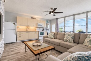 Eine moderne Küche mit Deckenventilator, einer Couch mit floralen Kissen und einem Essbereich mit einem Glastisch.