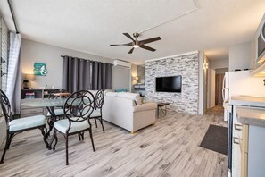 Ein modernes Wohnzimmer mit einer Couch, einem Esstisch, Stühlen, einem an einer Steinwand befestigten Fernseher und einem Deckenventilator.
