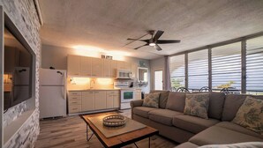 A modern kitchen with a dining area, a ceiling fan, and a large window with blinds. - Caribbean Blue Hideaway | 1BR Condo w/ Ocean View (Christiansted)