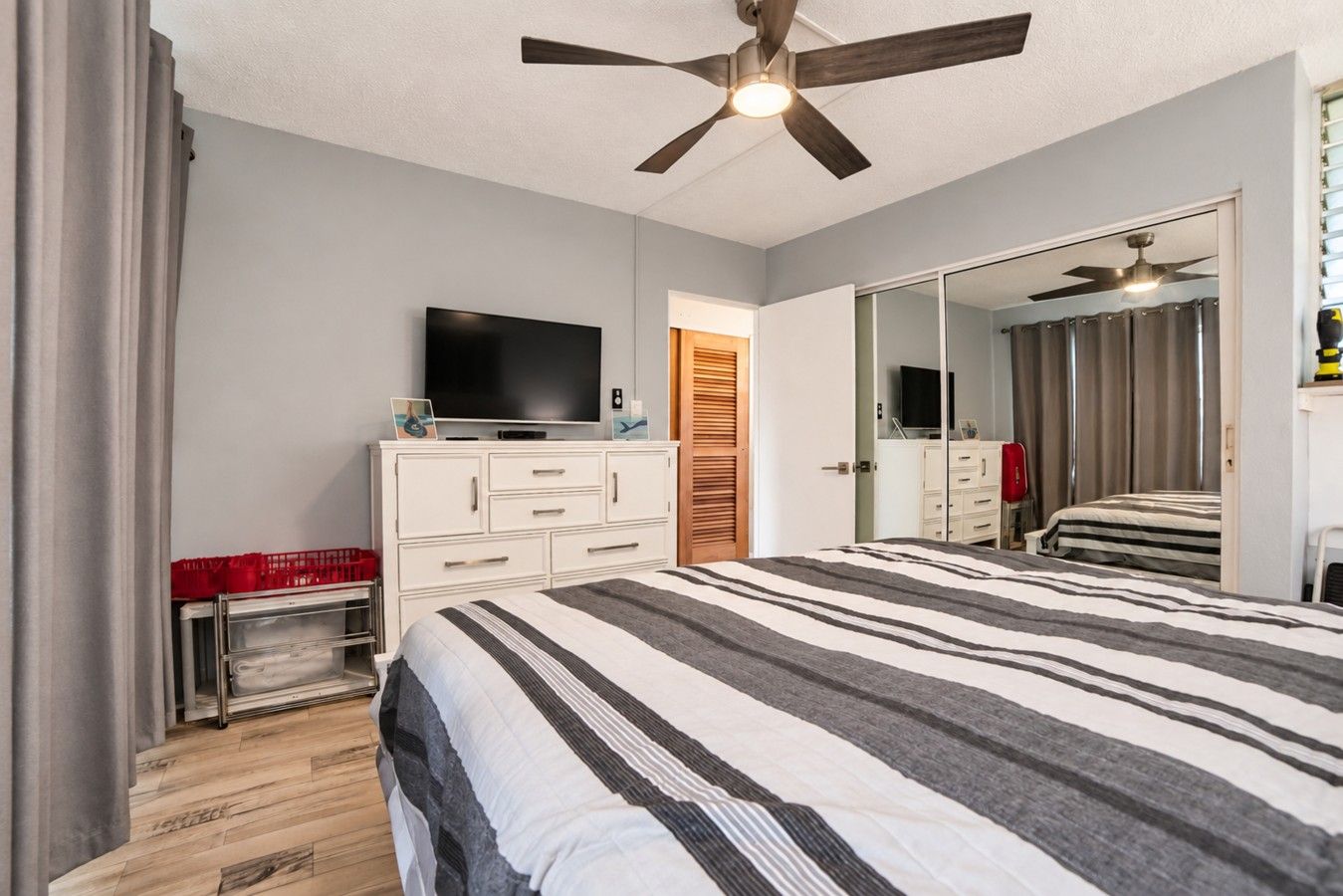 A bedroom with a bed, a TV, a wardrobe, a ceiling fan, and a mirror.