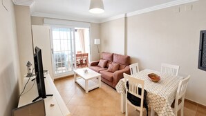 A living room with a sofa, a dining table with chairs, a TV, and a lamp. - Las Arenas T2 - Apartment with sea view (Isla Canela)