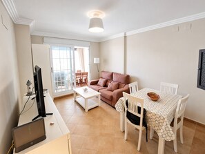 Ein Wohnzimmer mit einer Couch, einem Esstisch mit Stühlen, einem Fernseher und einer Lampe.