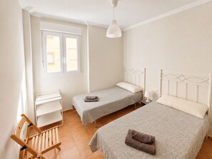 Ein Schlafzimmer mit zwei Einzelbetten, einem Schreibtisch, einem Stuhl und einem Fenster.