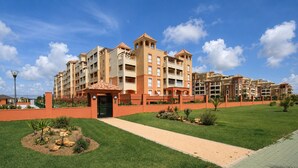A multi-story residential building with a central courtyard, a paved walkway, and a fenced perimeter. - Las Arenas T2 - Apartment with sea view (Isla Canela)