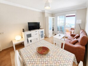 Ein modernes Wohnzimmer mit Flachbildfernseher, einem Esstisch mit gemustertem Tischläufer, einer Couch und einem Balkon mit Blick.