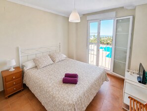 Ein Schlafzimmer mit einem Bett, einem Nachttisch, einem Schreibtisch und Blick ins Freie.