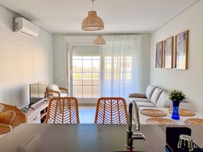 A modern living room with a sofa, chairs, a dining table, and a kitchen area. - Las Arenas T2 - Terrace with views (Ayamonte)