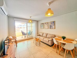 A living room with a sofa, a dining table with chairs, a coffee table, and a ceiling light fixture. - Las Arenas T2 - Terrace with views (Ayamonte)