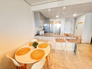 Eine moderne Küche mit weißen Schränken und einem Essbereich mit rundem Tisch und Korbstühlen.