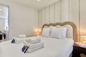A hotel room with a large bed, a wooden headboard, and a nightstand with a lamp. - Apartment in the Heart of the Marais (Paris)