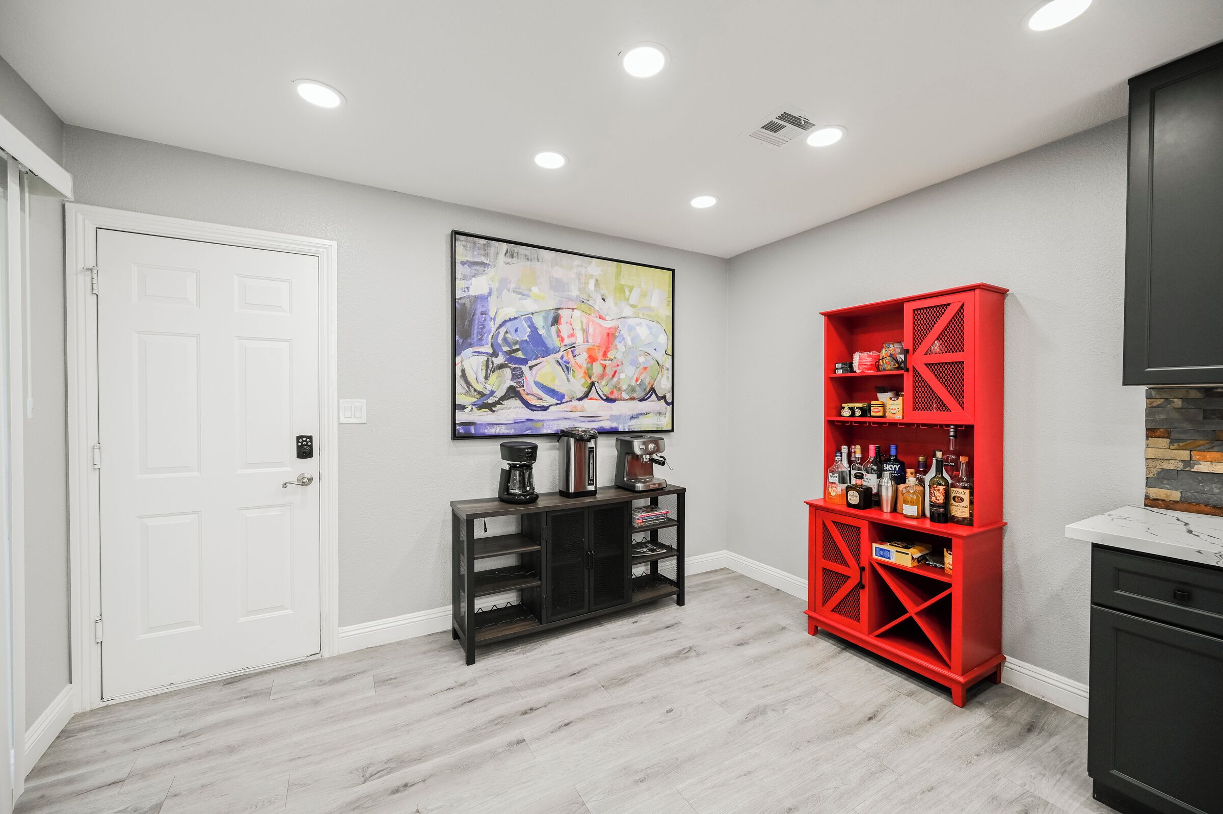 A modern kitchen with a white door, a red cabinet, and a large abstract painting on the wall.