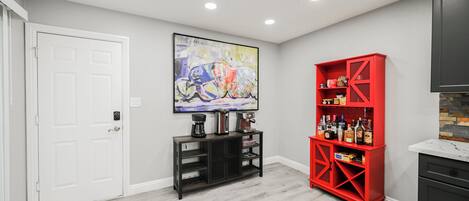 A modern kitchen with a white door, a red cabinet, and a large abstract painting on the wall.