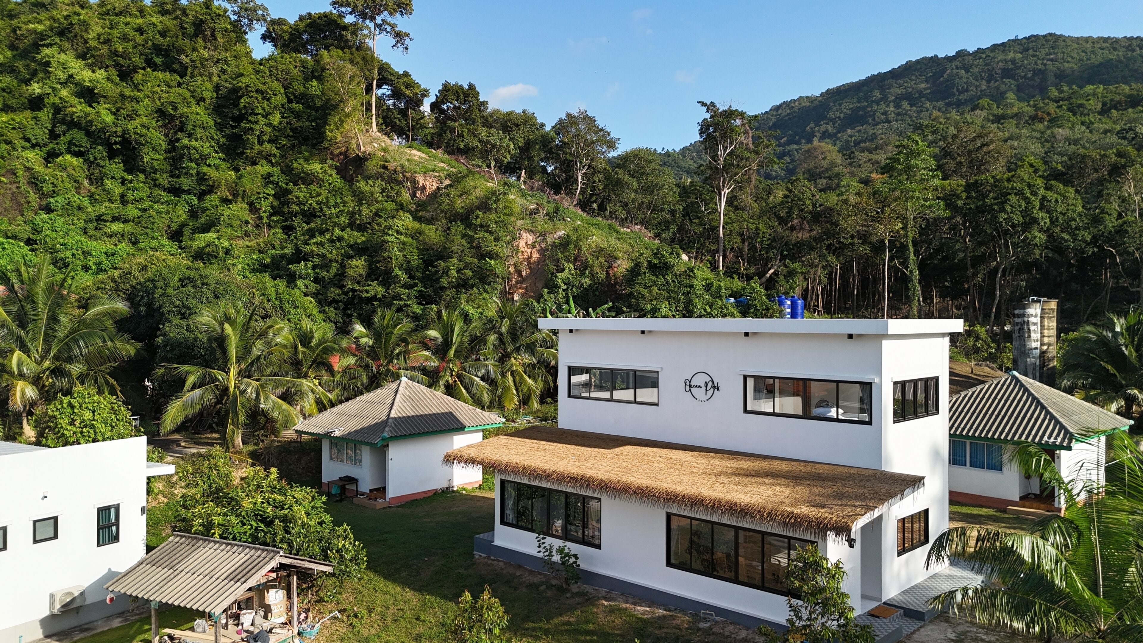A modern two-story building with large windows and a flat roof, surrounded by lush greenery and hills.