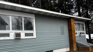 Una casa de un solo piso con revestimiento gris, un porche pequeño y un ventanal.