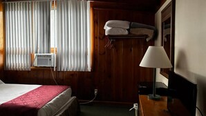 Habitación de hotel con cama, escritorio con lámpara, calentador de pared y ventana con persianas.