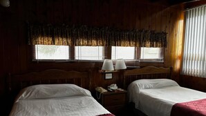 Una habitación con dos camas, una mesita de noche con lámpara y una ventana con persianas.