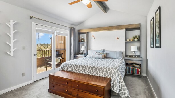 Quarto com cama, penteadeira, ventilador de teto e vista para um deck externo através de uma porta de correr.
