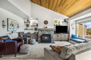 Ein modernes Wohnzimmer mit Kamin, Ledersofas, einem Flachbildfernseher und einem großen Fenster.