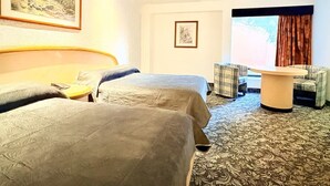 Una habitación de hotel con dos camas, una mesita, una silla y un ventanal con cortinas.