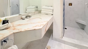 Un baño con lavamanos de mármol, un espejo, ducha con puerta de vidrio y un perchero para toallas.