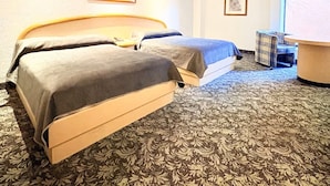 Habitación de hotel con dos camas, una mesita pequeña y una silla. Hay dos cuadros en la pared.