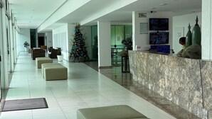 A modern hotel lobby with a reception desk, seating area, and a Christmas tree. - Luxor Tambau (João Pessoa)