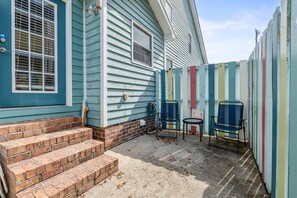 A house with a blue exterior, a brick entrance, and a fenced yard with colorful vertical panels. - Drift Away Pet Friendly Beach Side Town Home (Surfside)