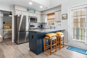 A modern kitchen with a central island, stainless steel appliances, and a view to the outside. - Drift Away Pet Friendly Beach Side Town Home (Surfside)