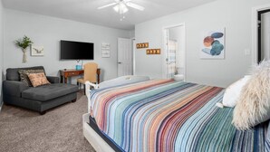 Une chambre à coucher comprenant un lit, un canapé, un bureau, une télévision et un ventilateur de plafond.