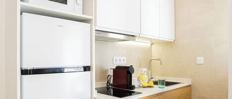 A compact kitchen with white cabinets, a built-in microwave, a coffee machine, and a sink.