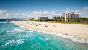 A beach with clear turquoise waters, a row of umbrellas, and a hotel in the background. - Marriott's Ocean Pointe 1 bedroom 12/13-12/17 (Palm Beach Shores)