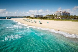 Una playa con aguas turquesas cristalinas, una hilera de sombrillas y un hotel al fondo.