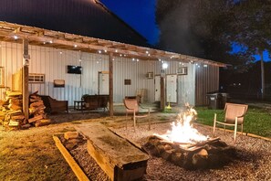 Ein rustikaler Sitzbereich im Freien mit Feuerstelle, Holzbänken und einer überdachten Terrasse mit Lichterketten.