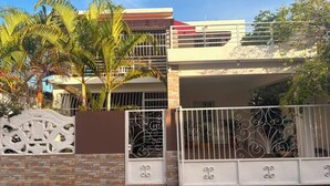 Una casa de dos pisos con entrada porticada, un balcón y un muro de ladrillo.