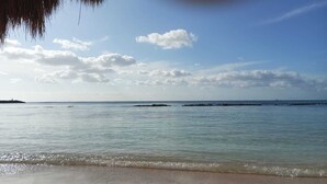 Ein Strand mit ruhigem Wasser, blauem Himmel und einer entfernten Küstenlinie.