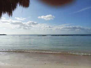 Ein Strand mit ruhigem Wasser, blauem Himmel und einer entfernten Küstenlinie.