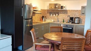 Eine kompakte Küche mit Kühlschrank, Mikrowelle und Herd. Ein Esstisch mit Stühlen und ein kleines Schrankchen sind ebenfalls vorhanden.