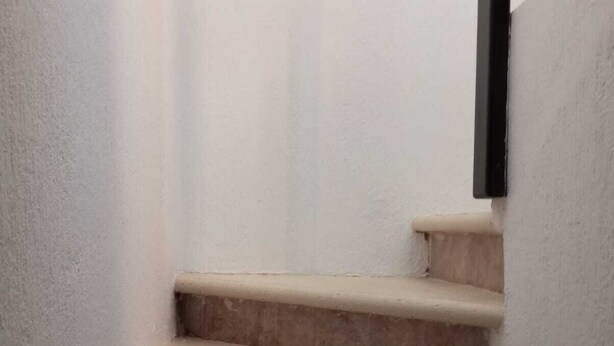 Beige Treppenstufen mit einem schwarzen Geländer, die zu einer höheren Ebene führen.