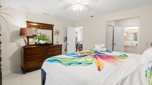 Quarto com cama, cômoda, espelho, ventilador de teto e vista para o banheiro.