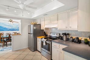 A modern kitchen with stainless steel appliances, light wood cabinetry, and a dining area with a view of the ocean. - New Game Room, Saltwater Pool, 15 min to Beach. Grill, Corhole, Big Fenced Yard (Clearwater)
