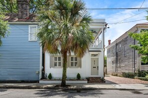 Ein zweigeschossiges Haus mit weißer Haustür, einer kleinen Veranda und einer Palme im Vorgarten.