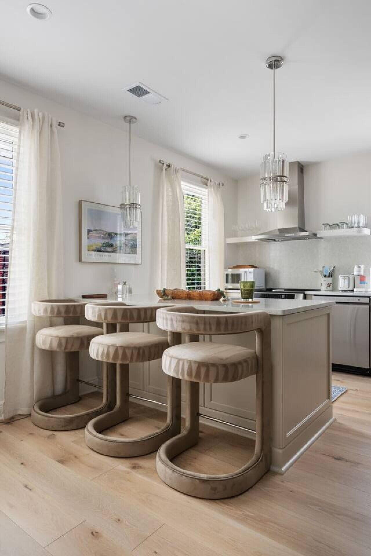 A modern kitchen with a central island, bar stools, and pendant lighting.