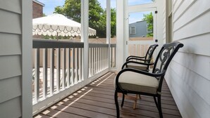 Eine überdachte Veranda mit weißer Brüstung, zwei Stühlen und einem weißen Sonnenschirm.