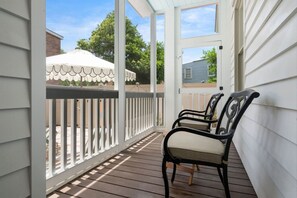 Eine überdachte Veranda mit weißer Brüstung, zwei Stühlen und einem weißen Sonnenschirm.