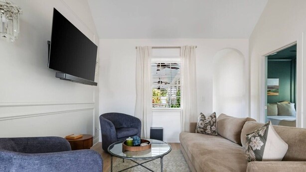 Ein Wohnzimmer mit Flachbildfernseher, einem grauen Sessel, einem beigen Sofa und einem kleinen Couchtisch mit Dekoration.