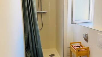 Une salle de bain avec une douche, des toilettes et une petite étagère en bois.