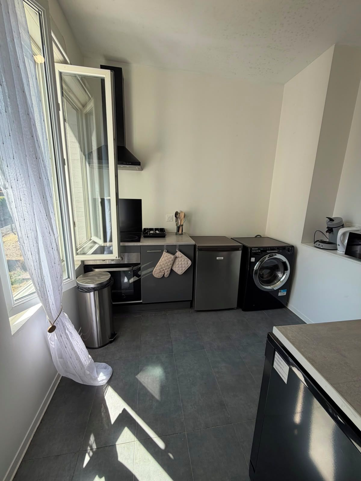 Cocina compacta con lavavajillas, lavadora y ventana con cortinas.