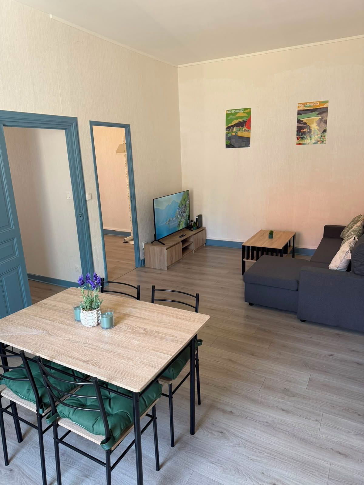 Een woonkamer met een eethoek, een bank, een televisie en kunstwerken aan de muur.