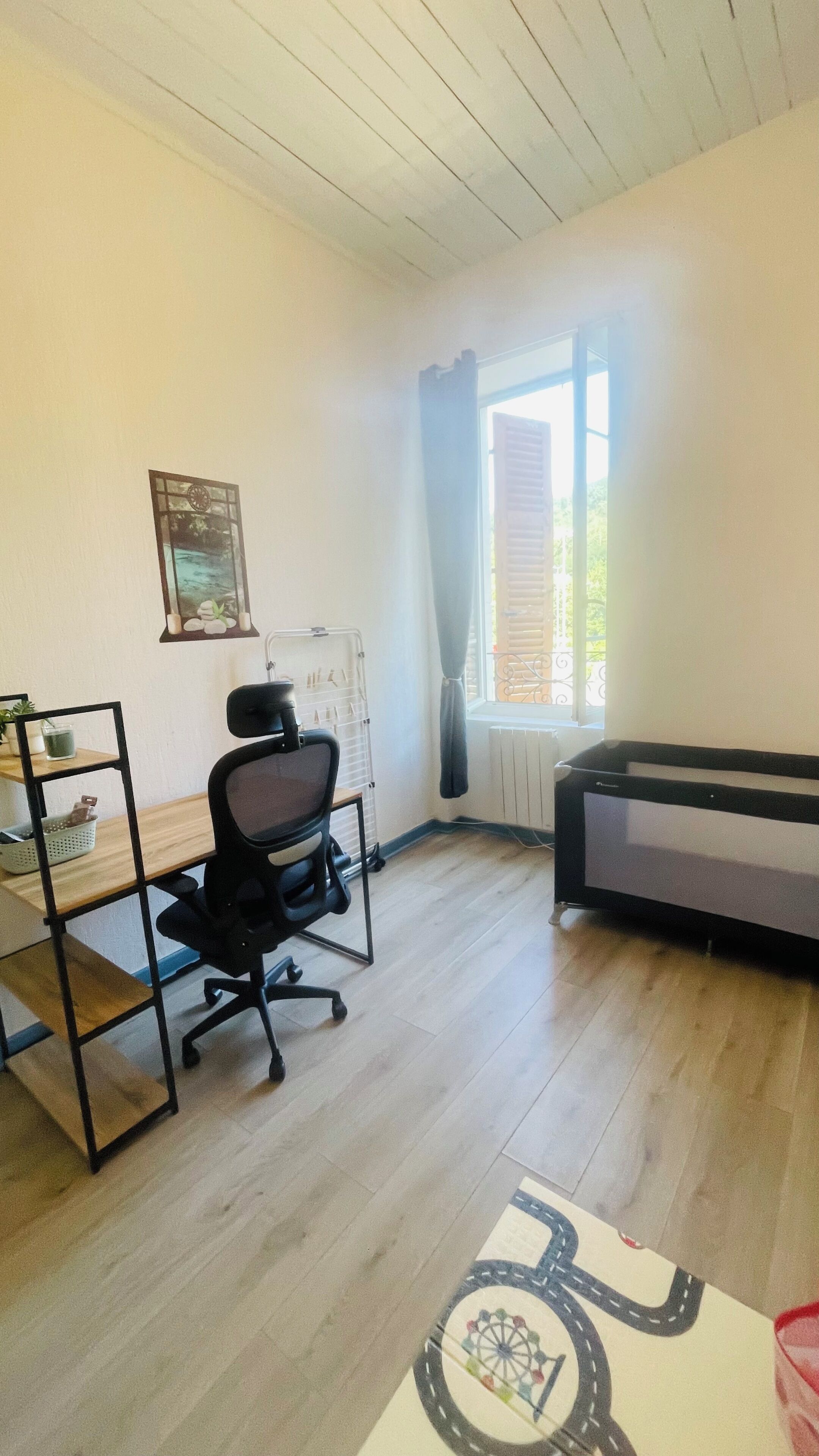 Ein Zimmer mit Schreibtisch, Stuhl, Heizkörper, einem Fenster mit Vorhängen und einem Sofa.
